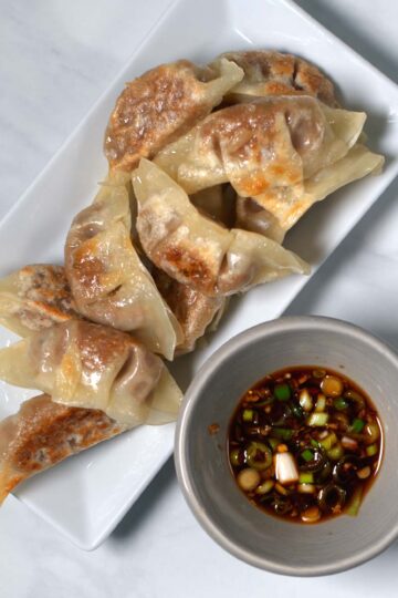 A serving of dumplings on a plate with a serving bowl of Gyoza Sauce.