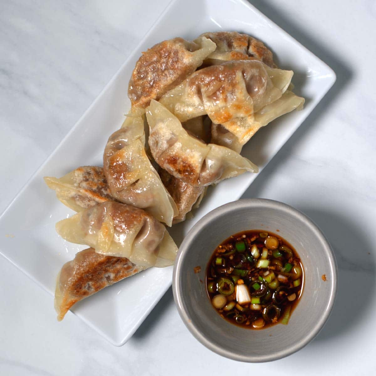A serving of dumplings on a plate with a serving bowl of Gyoza Sauce.