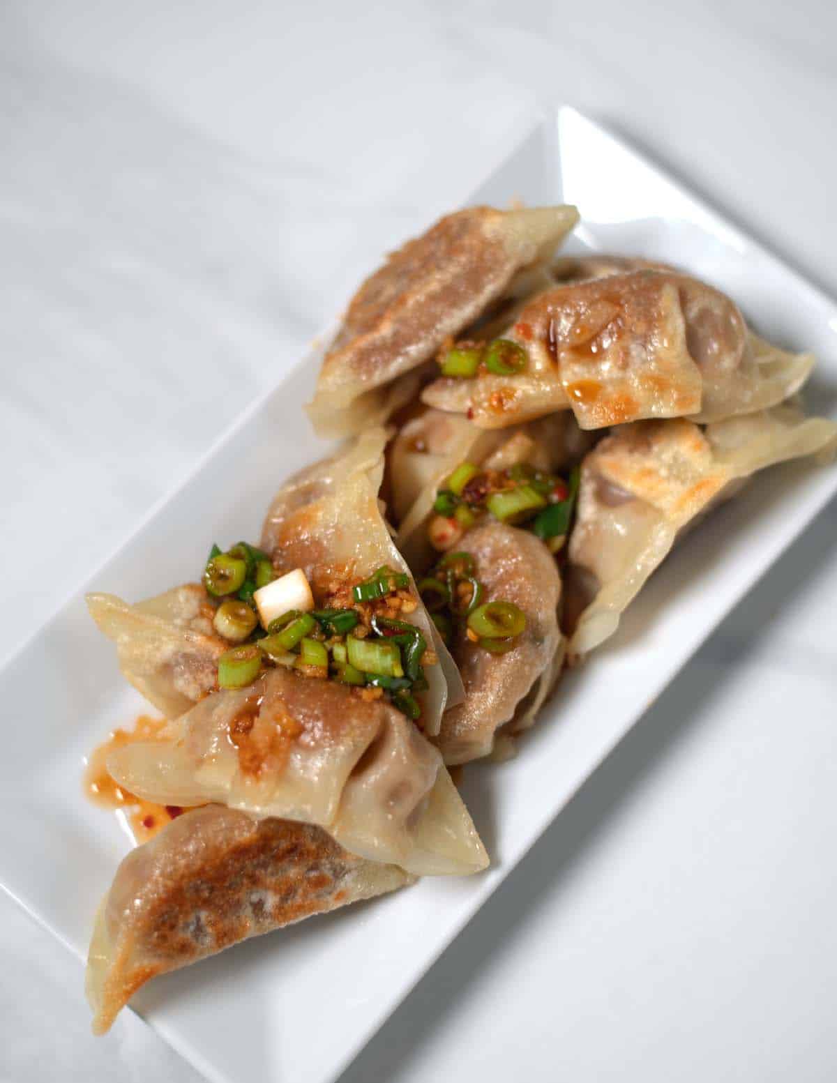 Gyoza Sauce has been poured over fumplings on a plate.