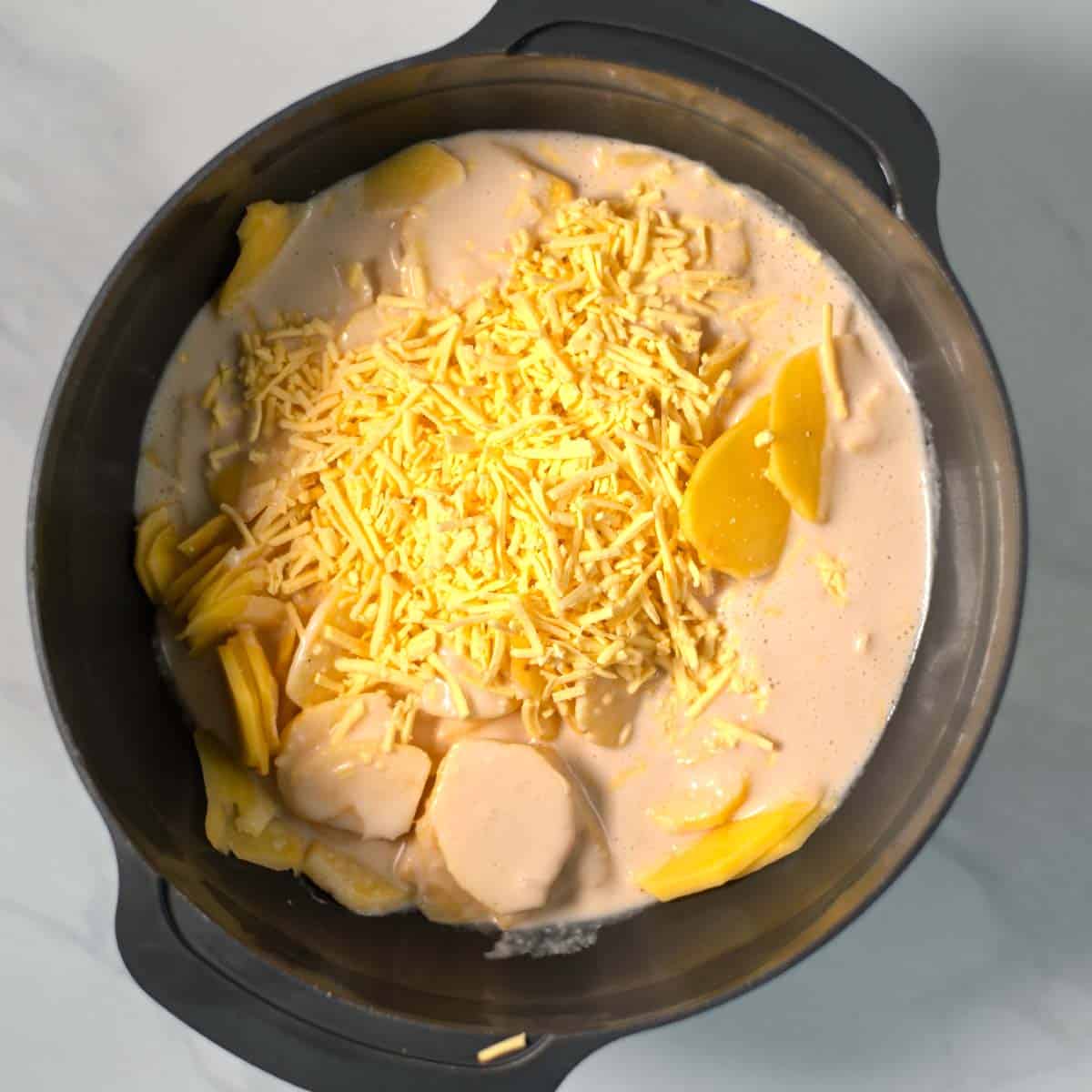 Potato slices, sauce, and half of the cheese are mixed in a large serving bowl.