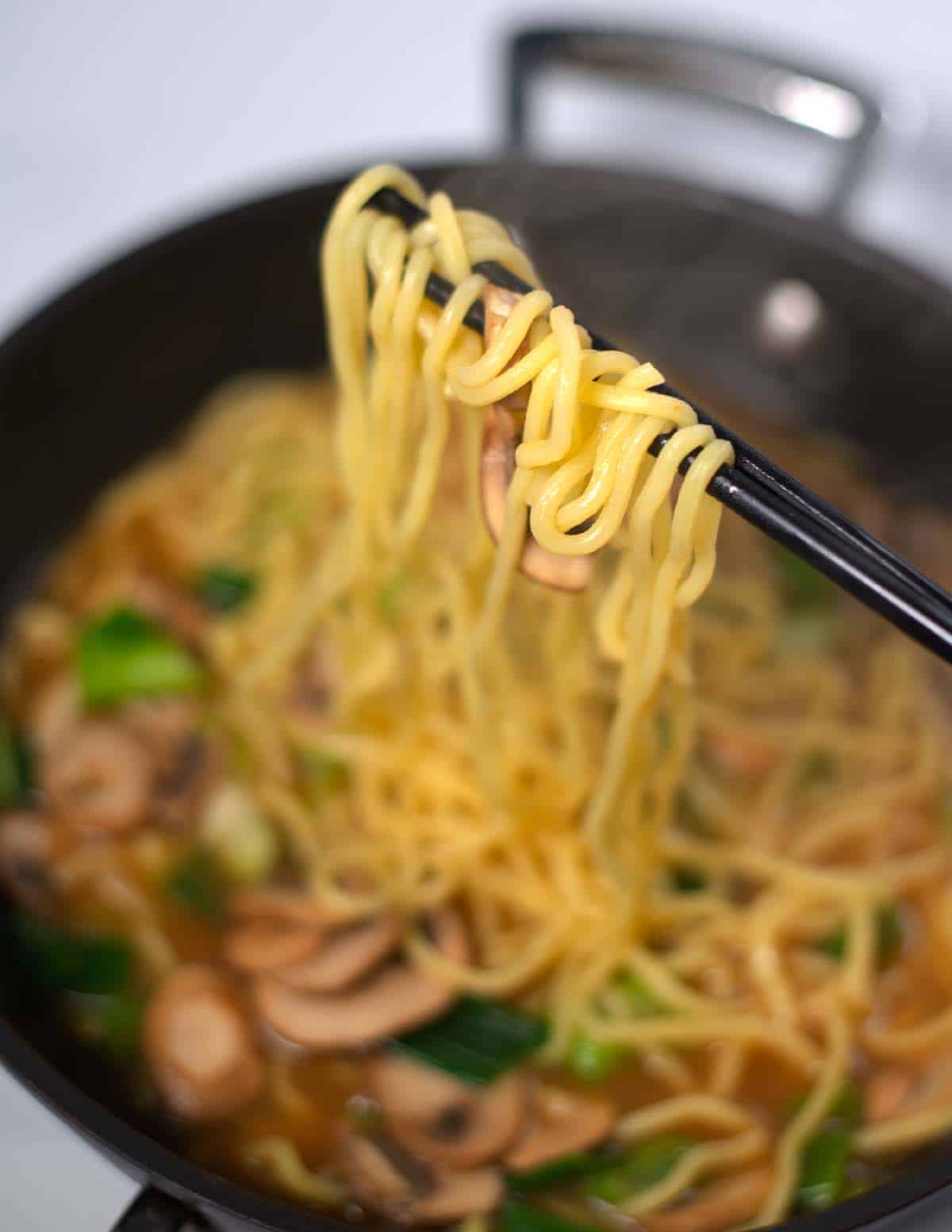 Chopsticks lift noodles from Ramen.