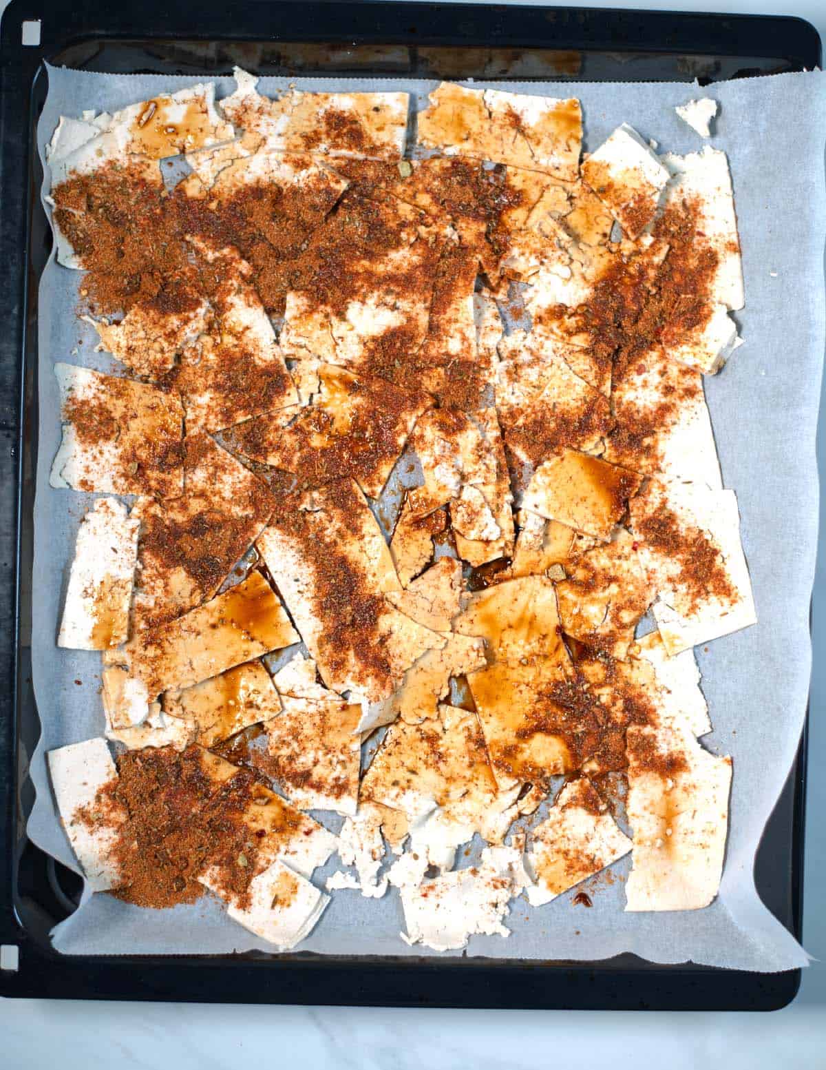 Shaved tofu with seasoning on a baking sheet.