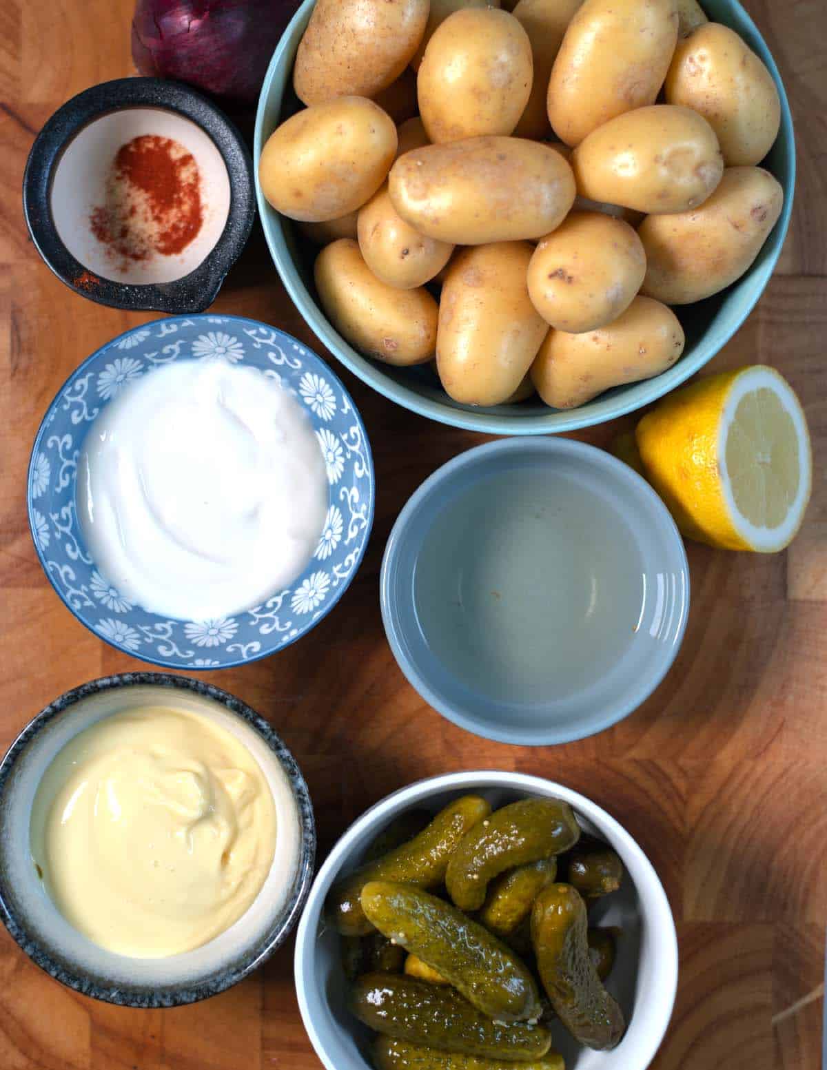 Ingredients needed to make Smashed Potato Salad are collected on a wooden cutting board before preparation.