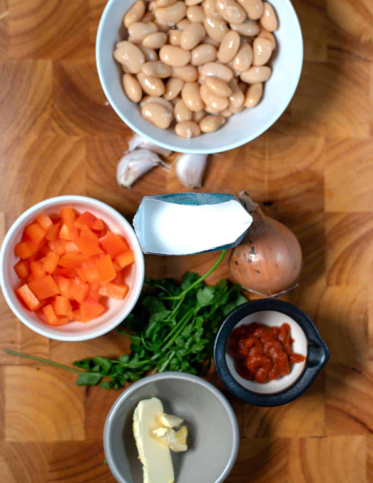 Ingredients needed to make Creamy Harissa Butter Beans are collected on a wooden board.