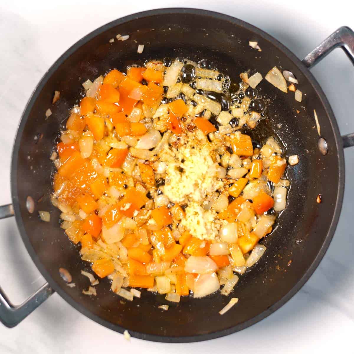 Onions and diced bell pepper are roasted in a pan.