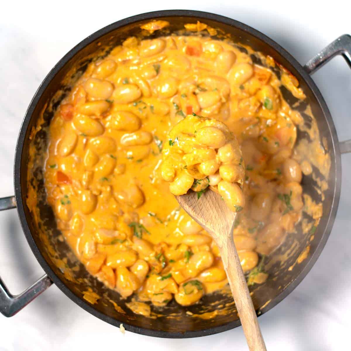 A wooden spoon lifts Creamy Harissa Butter Beans.