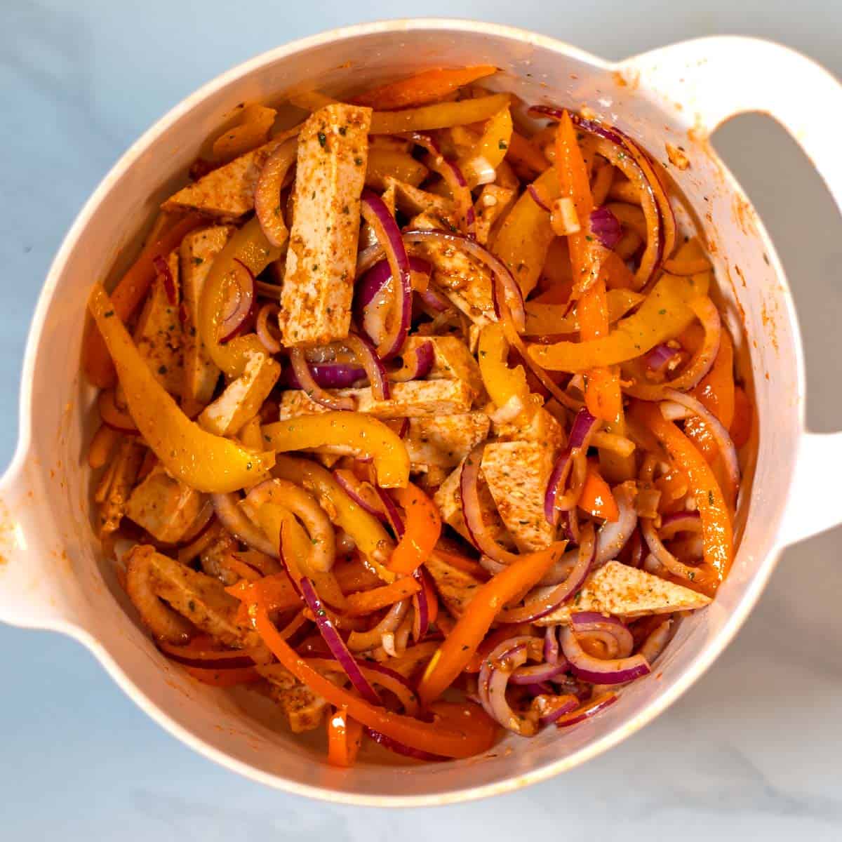 Tofu, onions, bell pepper mixed with seasoning in a pan.
