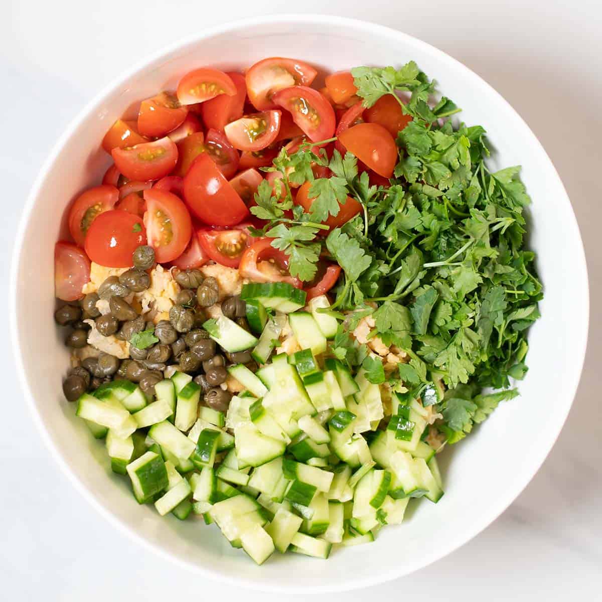 The salad ingredients in a large white mixing bowl bowl.