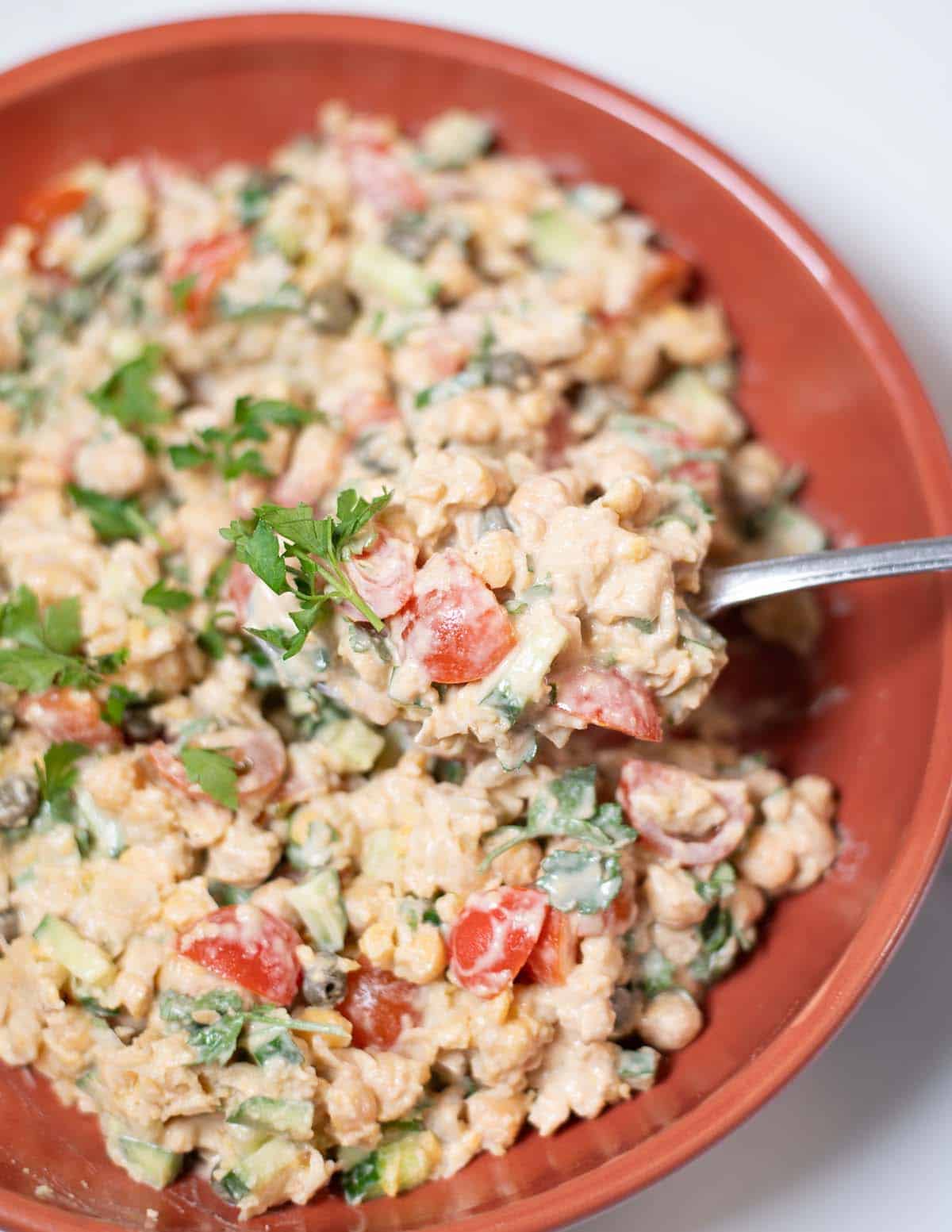 A large spoon lifts Smashed Chickpea Salad from the plate.