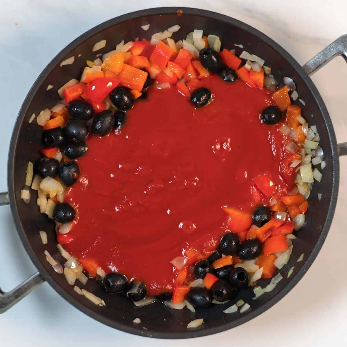 Tomato sauce with vegetables and olives is prepared in a sauce pan.