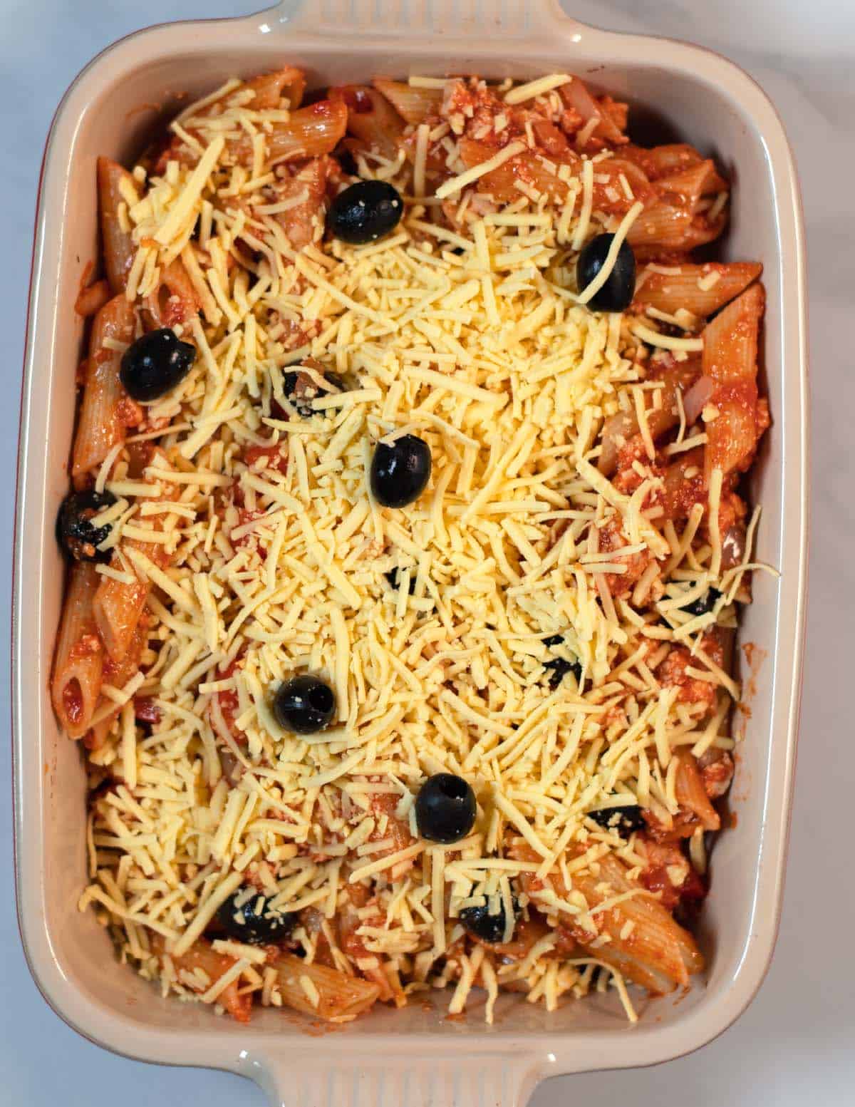 The Tofu Pasta Casserole in a baking dish, covered with vegan cheese, before baking.