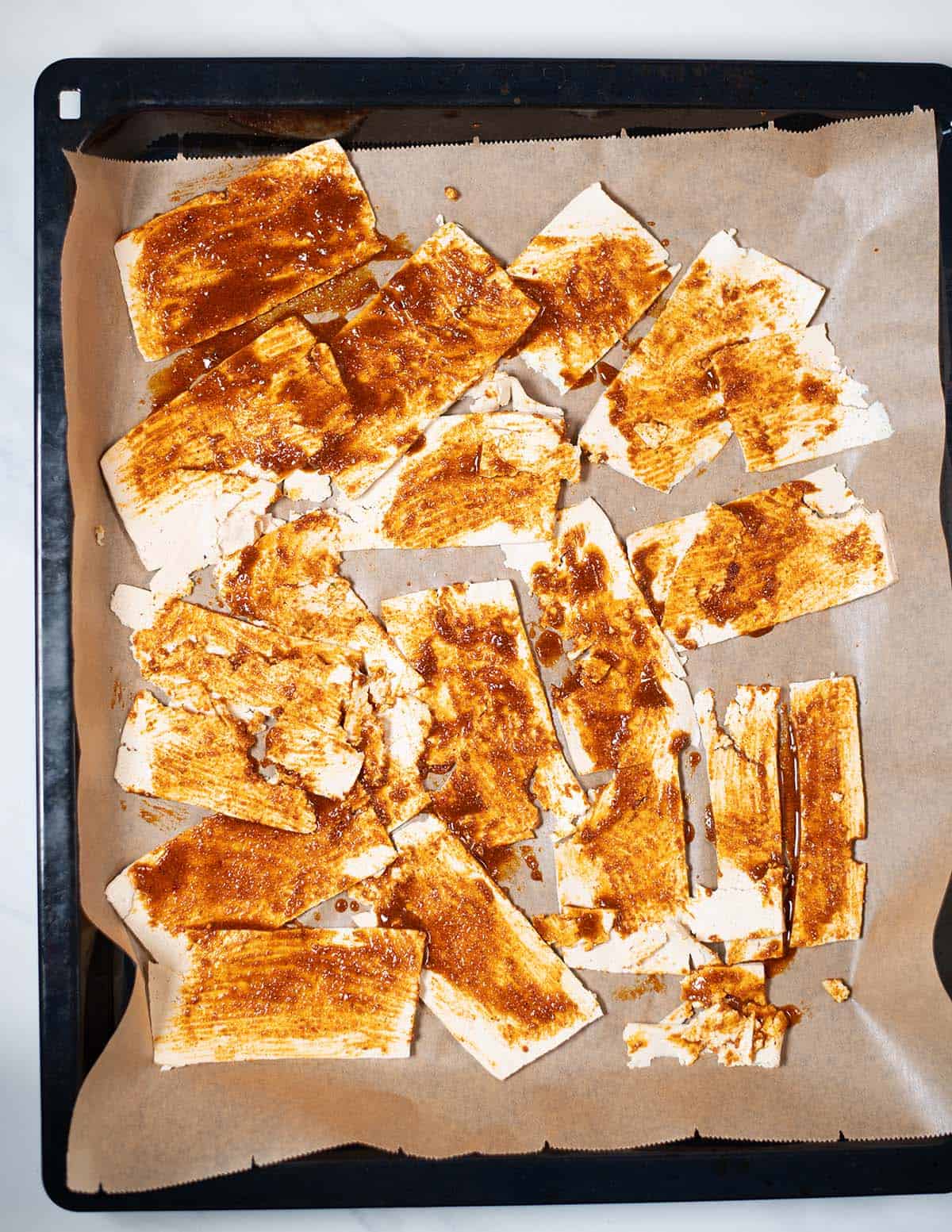 Tofu slices rubbed in Shwarama spices on a baking sheet before baking.