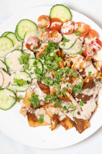 A large serving of Tofu Shawarma with cucumbers and tomatoes, garnished with tahini sauce.
