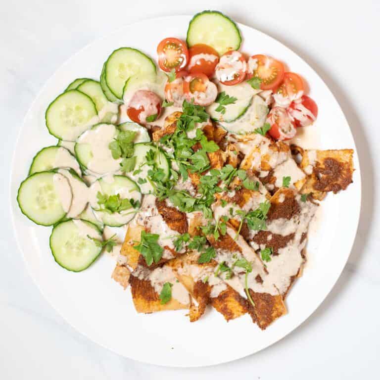 A large serving of Tofu Shawarma with cucumbers and tomatoes, garnished with tahini sauce.