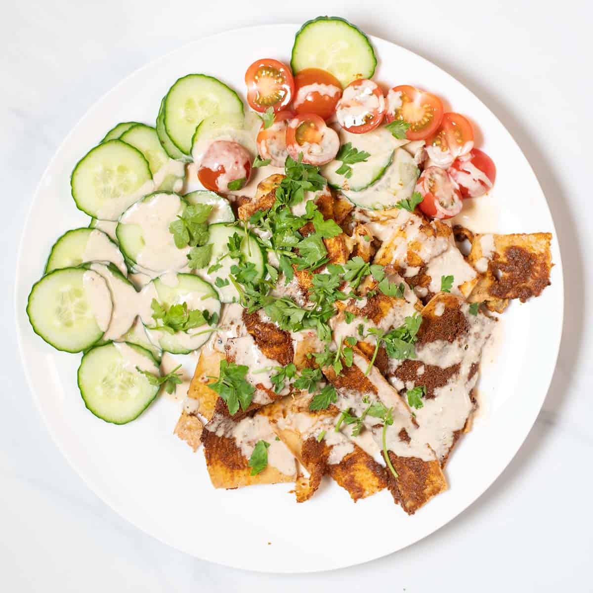 A large serving of Tofu Shawarma with cucumbers and tomatoes, garnished with tahini sauce.