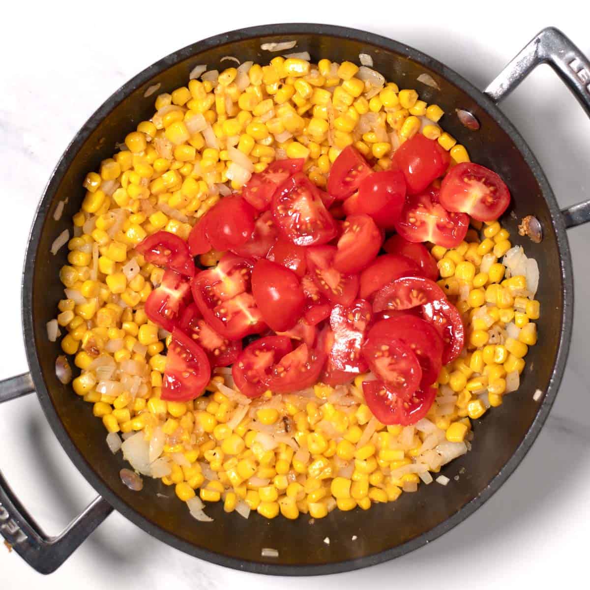 Onions, corm, and tomatoes in a frying pan.