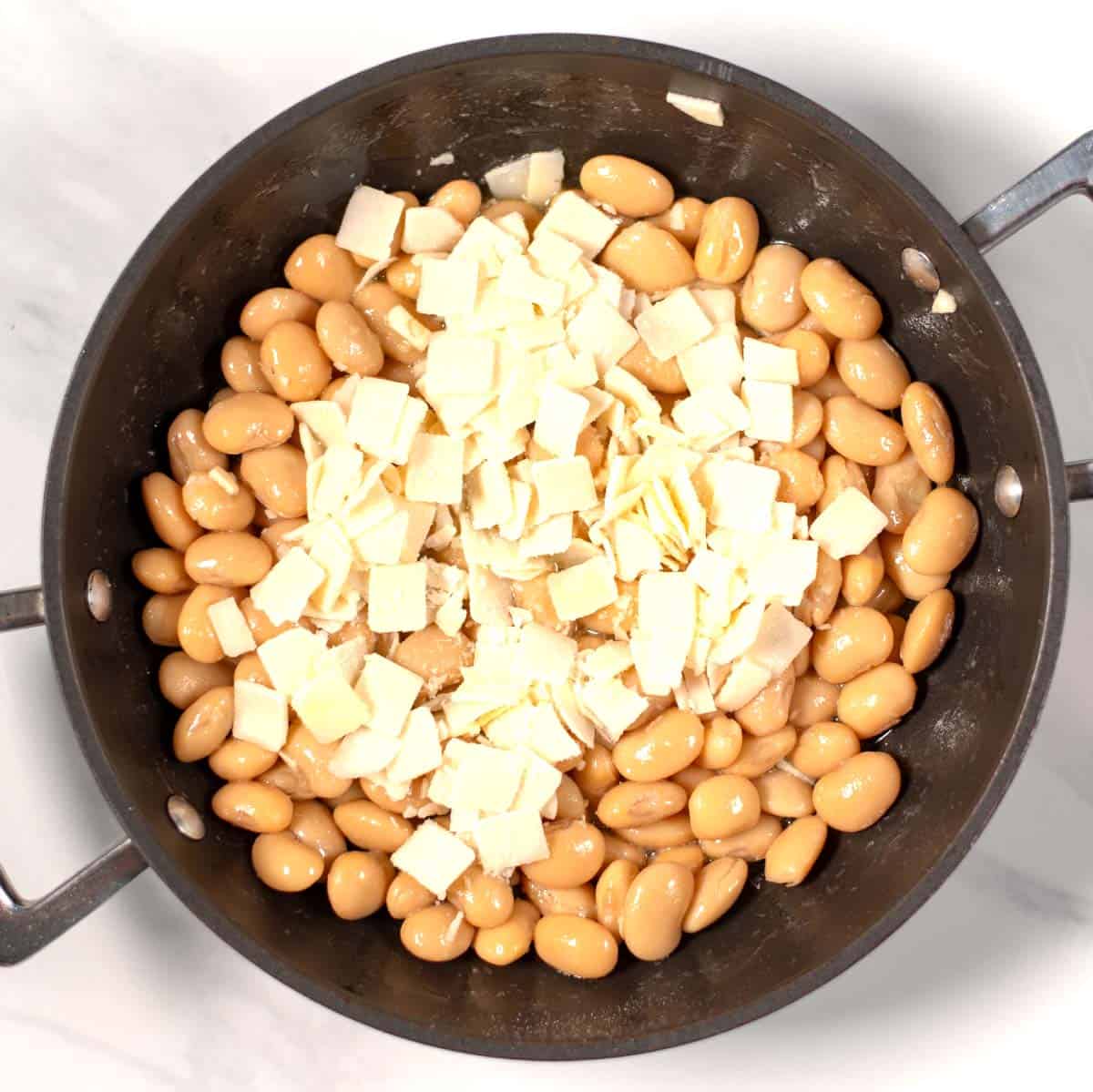 Vegan parmesan is added to beans in the pan.