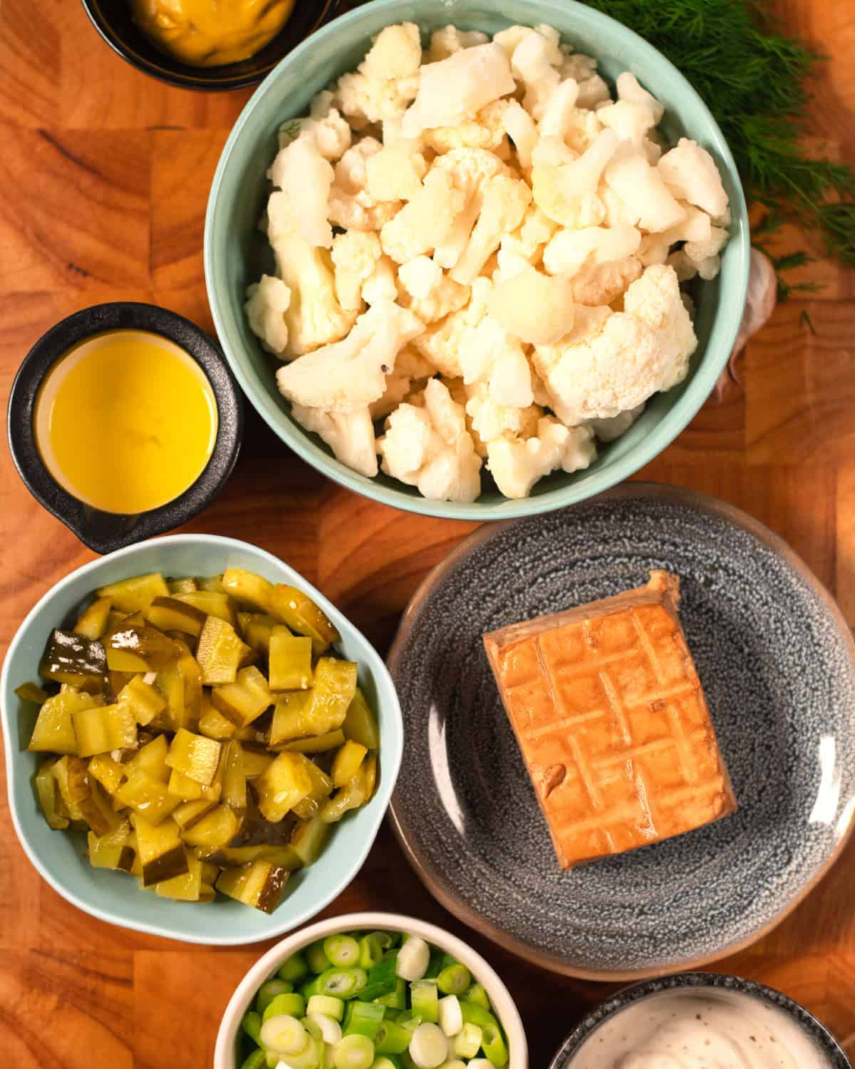 Ingredients needed to make Cauliflower Potato Salad are collected on a cutting board.