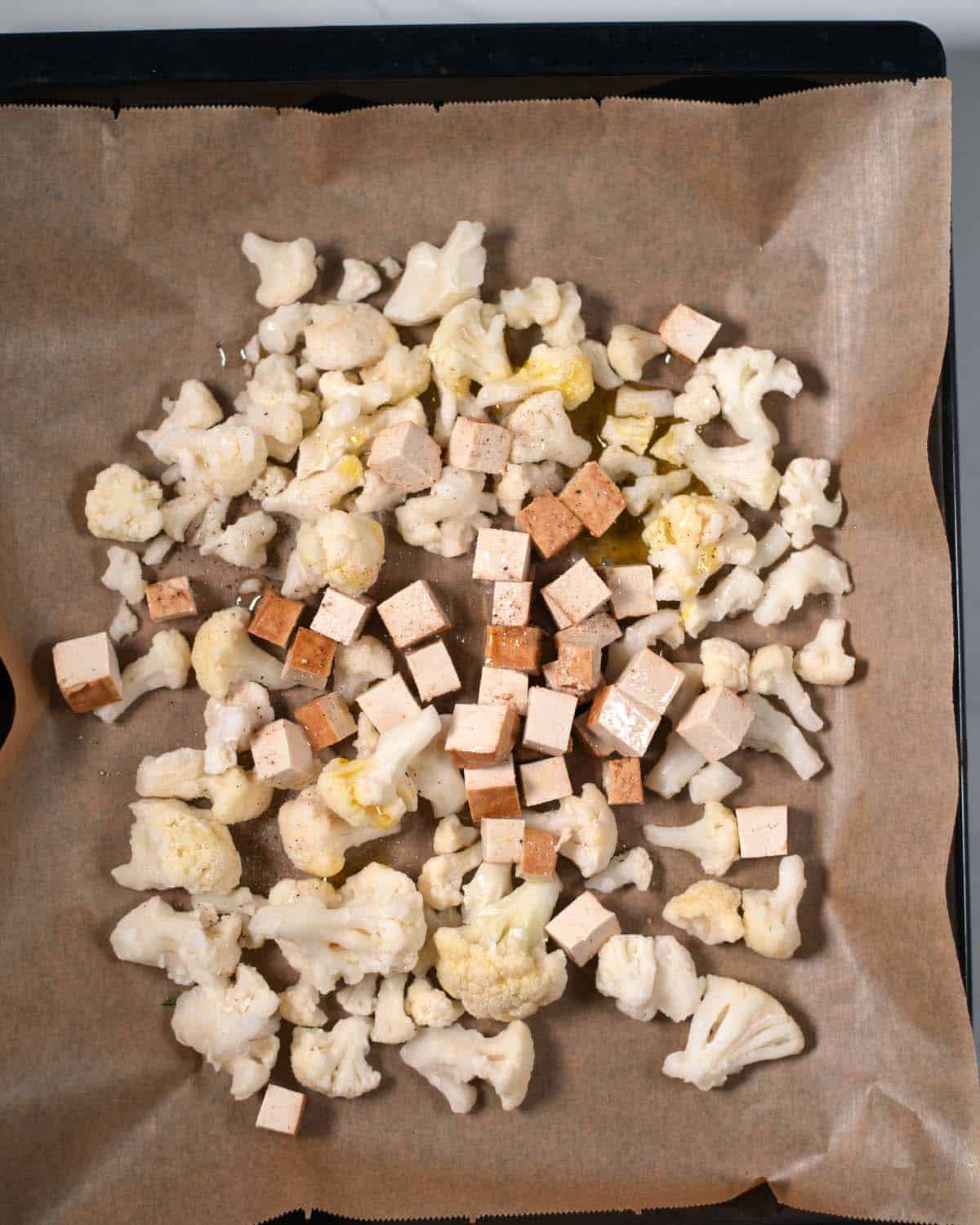 Cubed tofu and cauliflower on a baking sheet before roasting.
