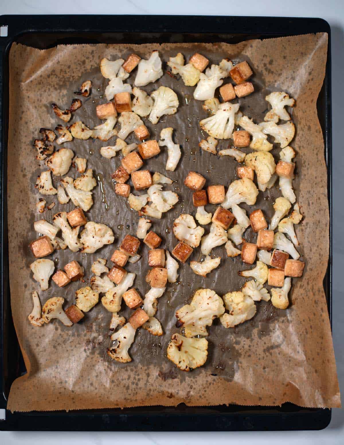 Cubed tofu and cauliflower on a baking sheet after oven roasting.