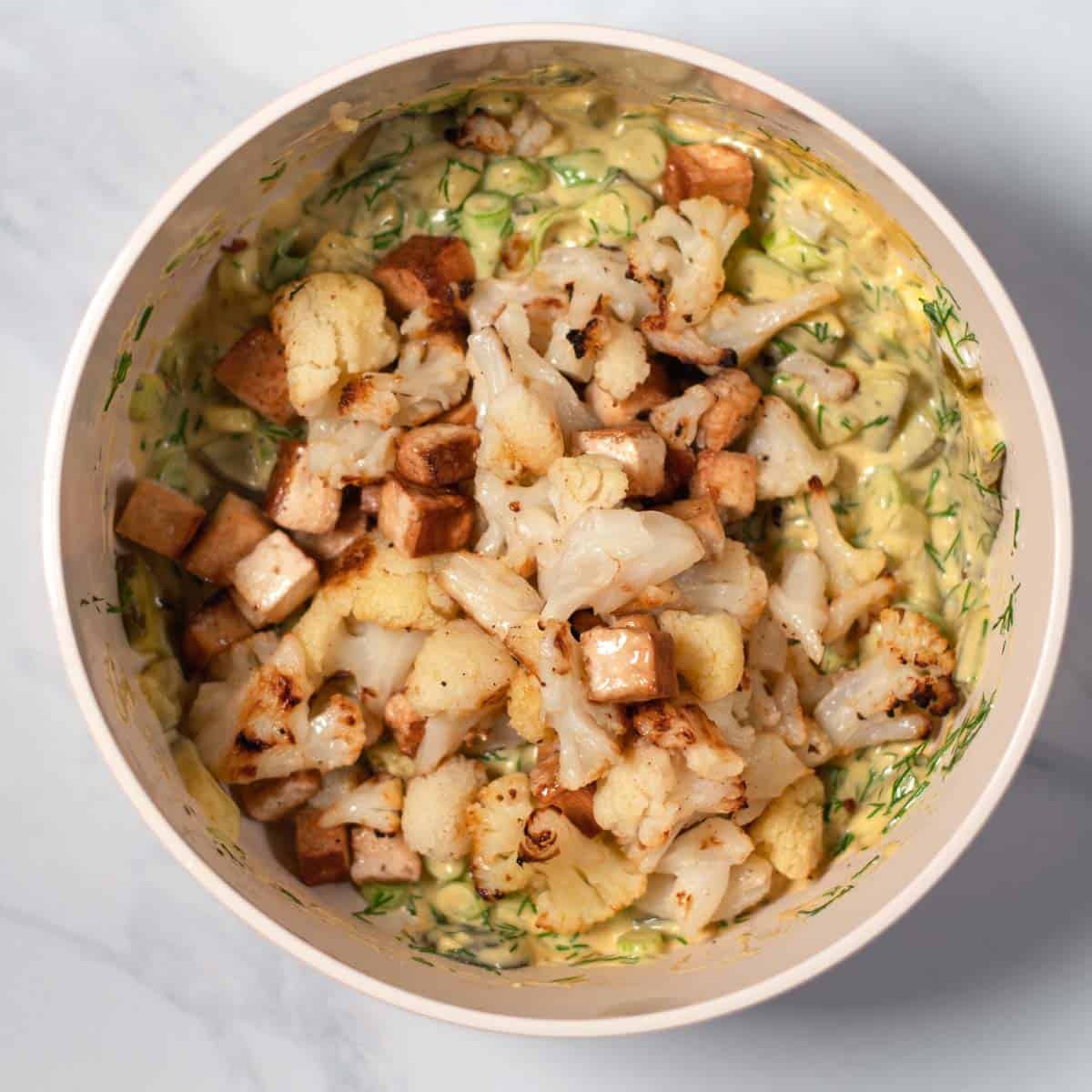 Roasted tofu and cauliflower are given to the bowl with the dressing for the Cauliflower Potato Salad.