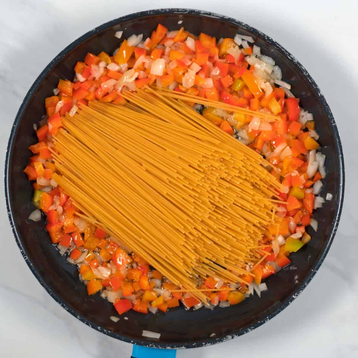 Raw pasta is given to a pan with onions and bell pepper.