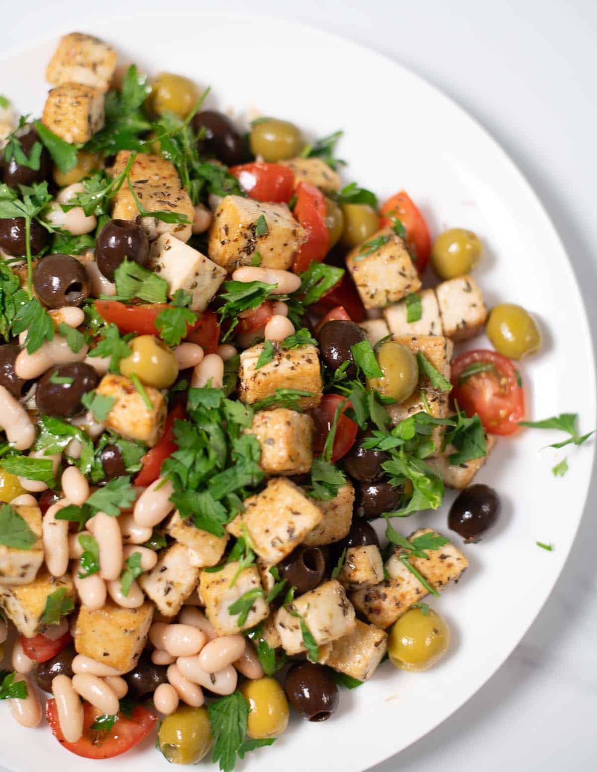 Vibrant olive salad with white beans, cherry tomatoes, and crispy tofu pieces.