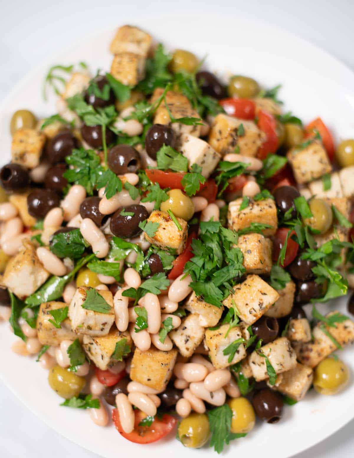 Vibrant olive salad with white beans, cherry tomatoes, and crispy tofu pieces.