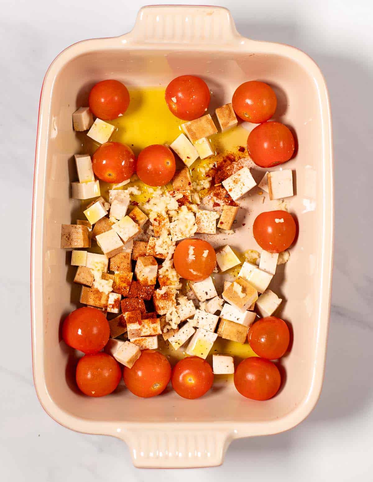 A baking dish with smoked tofu, tomatoes and spices, tossed in olive oil.