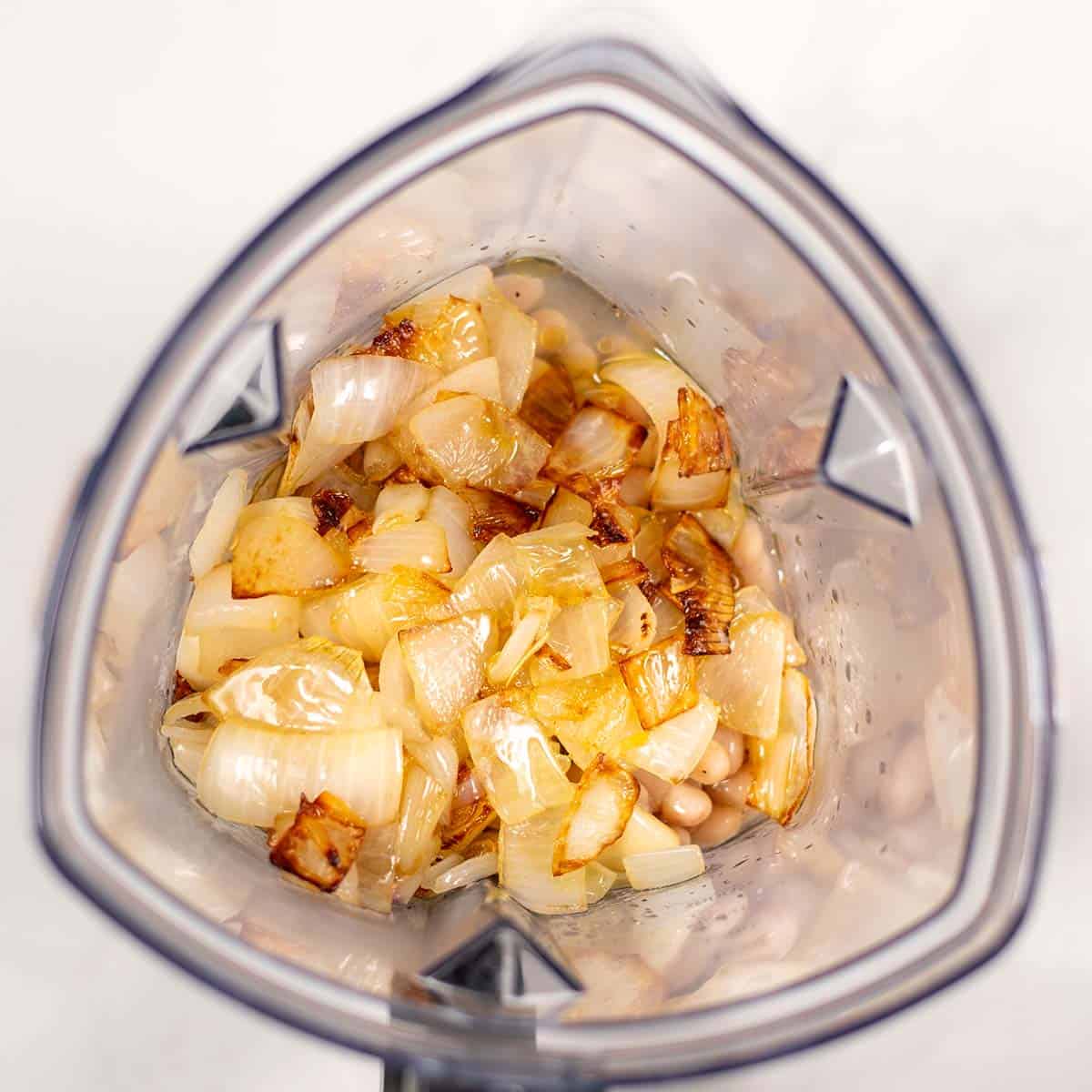 Roasted onions and garlic are given to the bowl of a blender with lemon juice, white beans and vegetable broth.