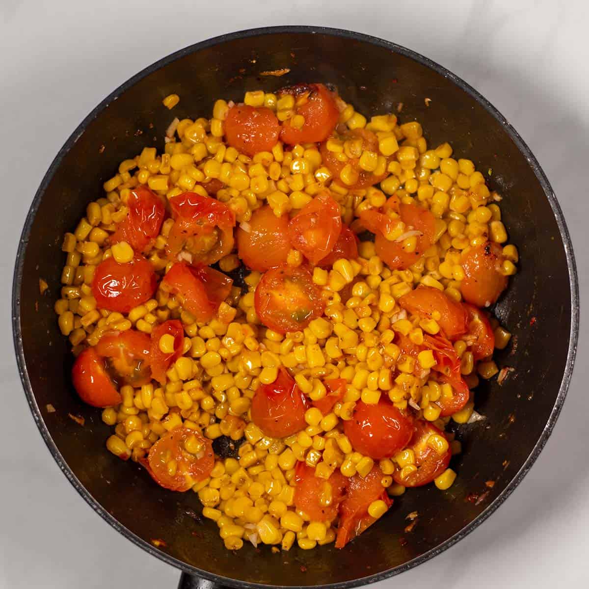 Corn and tomatoes are roasted in a pan.