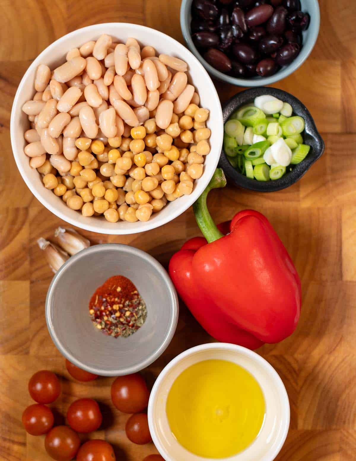 Ingredients needed for making Dense Bean Salad are collected on a wooden board.