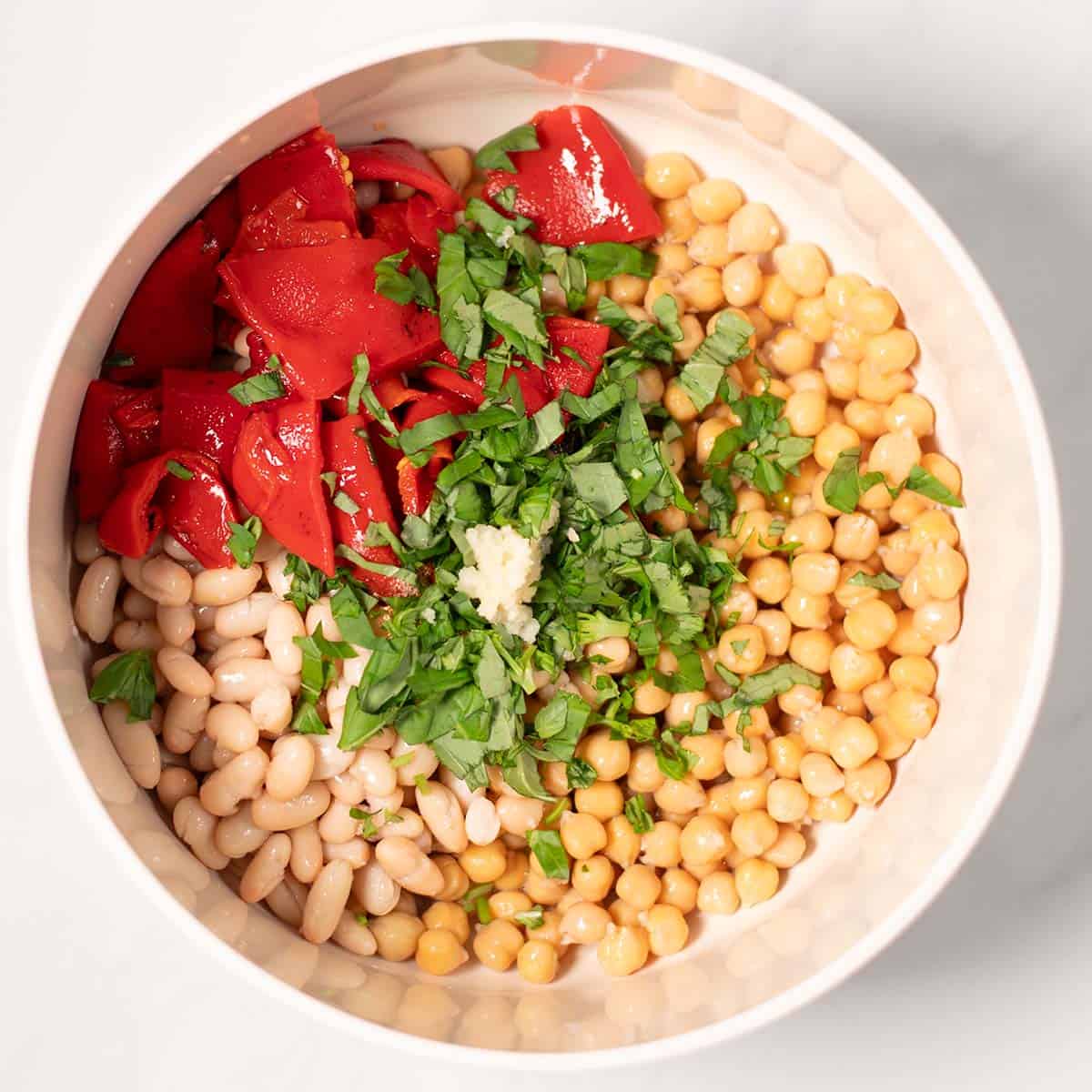Beans, chickpeas, basil, red peppers are given to amixing bowl.
