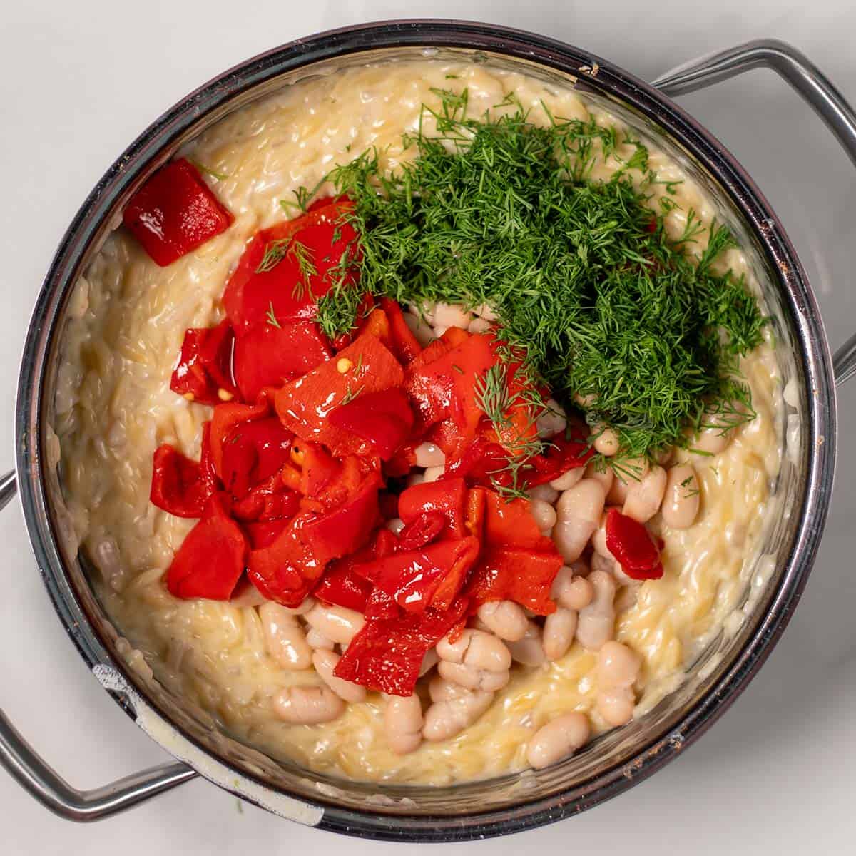 Red bell peppers and dill are mixed with the cooked creamy orzo.