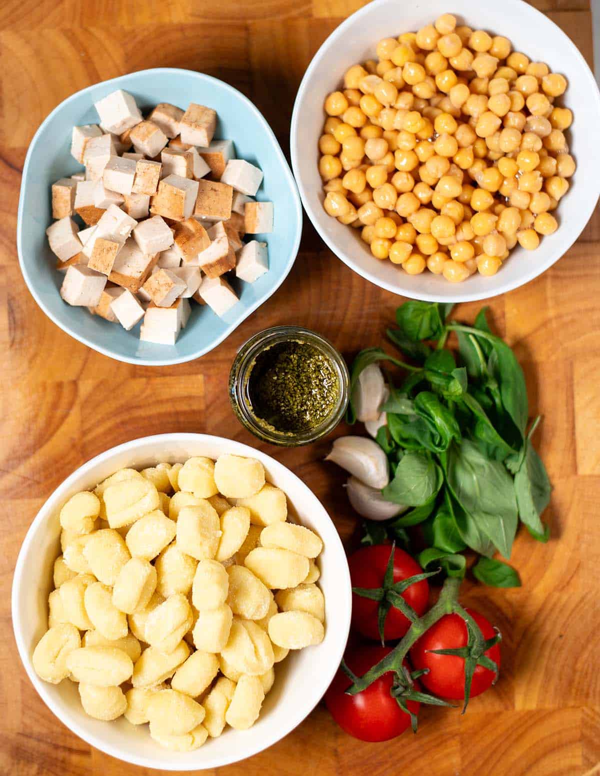 Ingredients needed for making Pesto Gnocchi are collected on a wooden board.