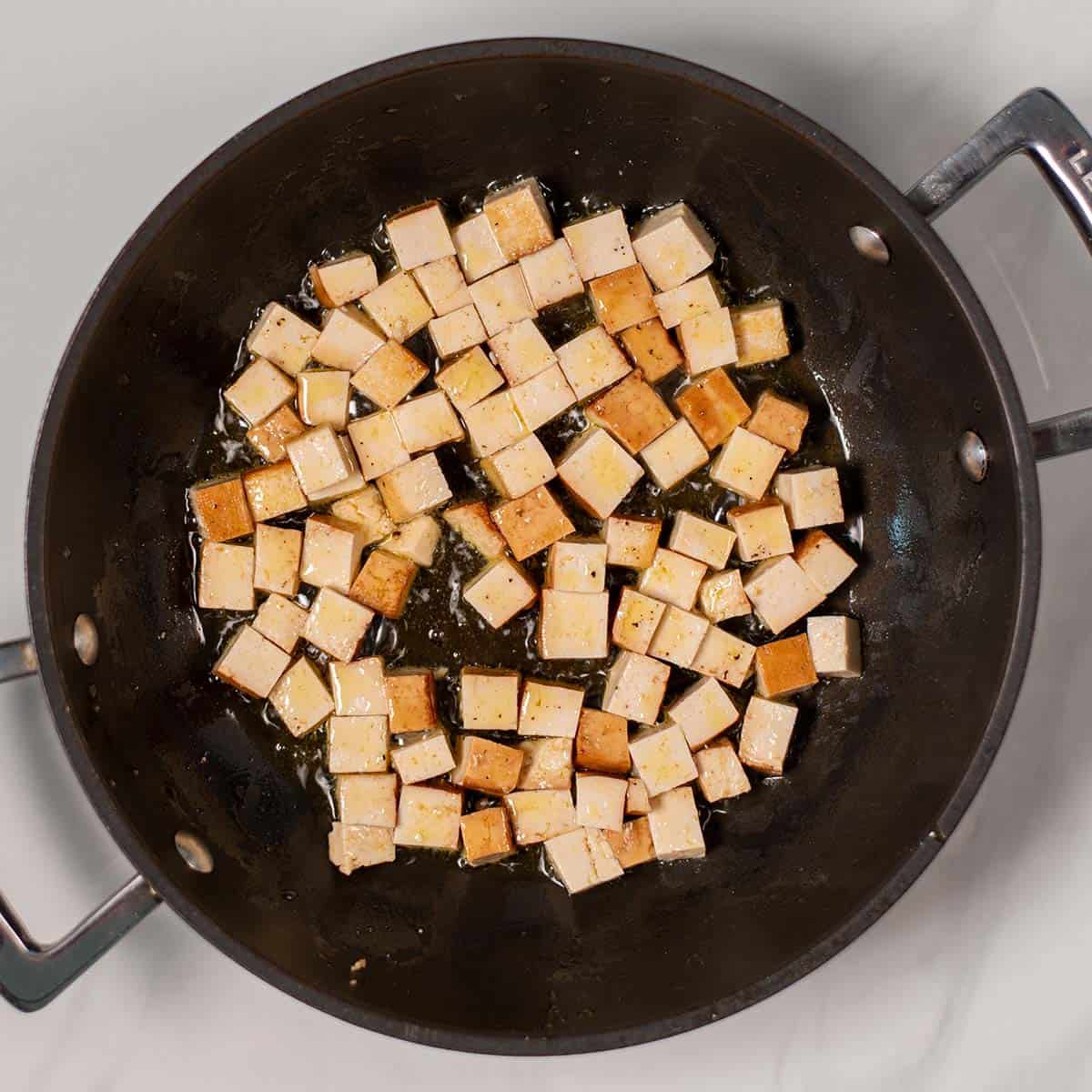 Small smoked tofu cubes are fried in a pan.