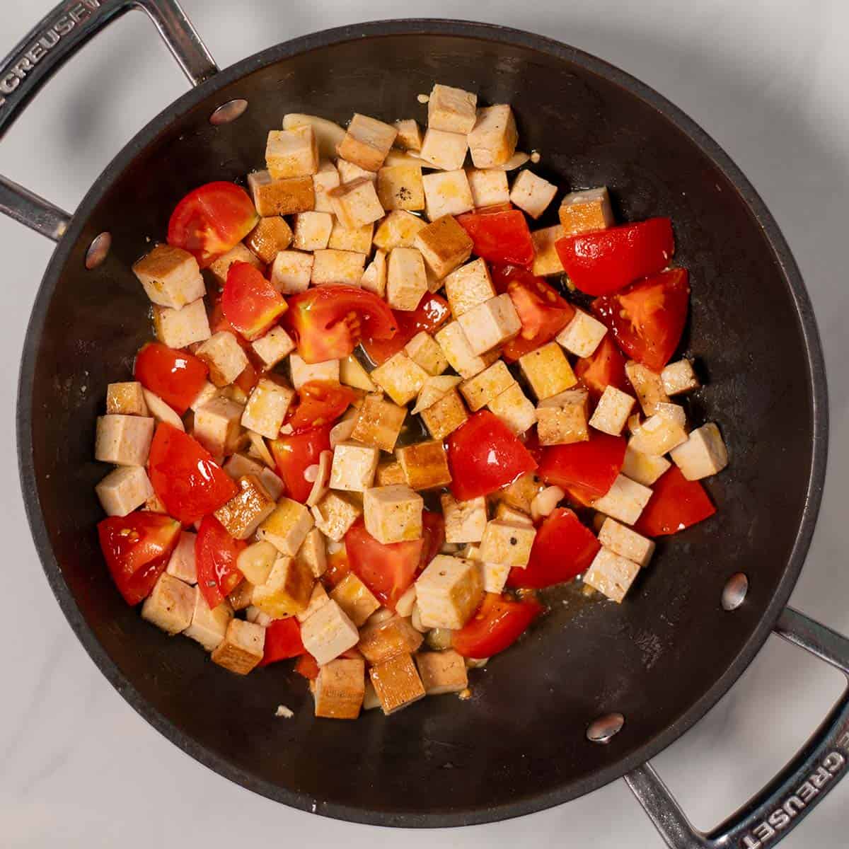 Quartered tomatoes and garlic are given to the frying pan with smoked tofu.