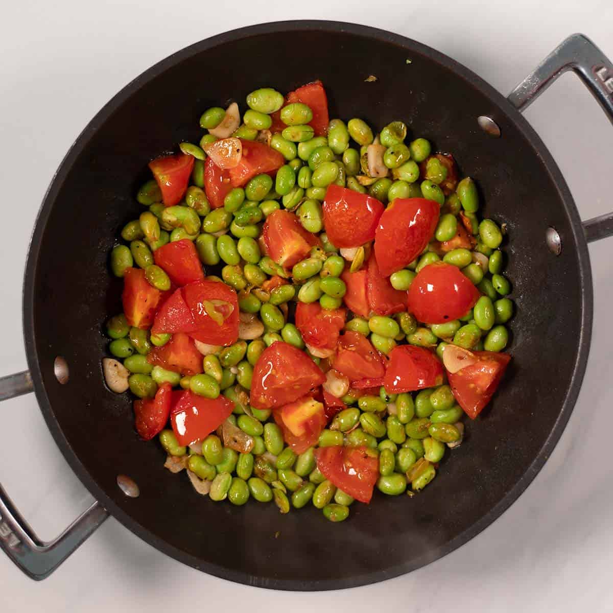 Edamame, tomatoes and garlic being fried.
