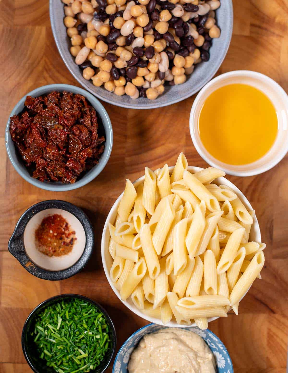 Ingredients needed to make Three Bean Pasta Salad are collected before the preparation on a wooden cutting board.