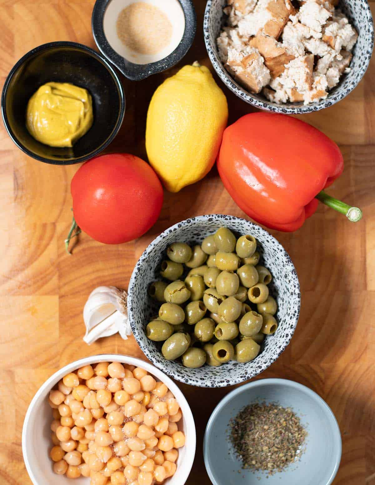 Ingredients needed to make Chopped Salad Sandwich are collected on a wooden cutting board.