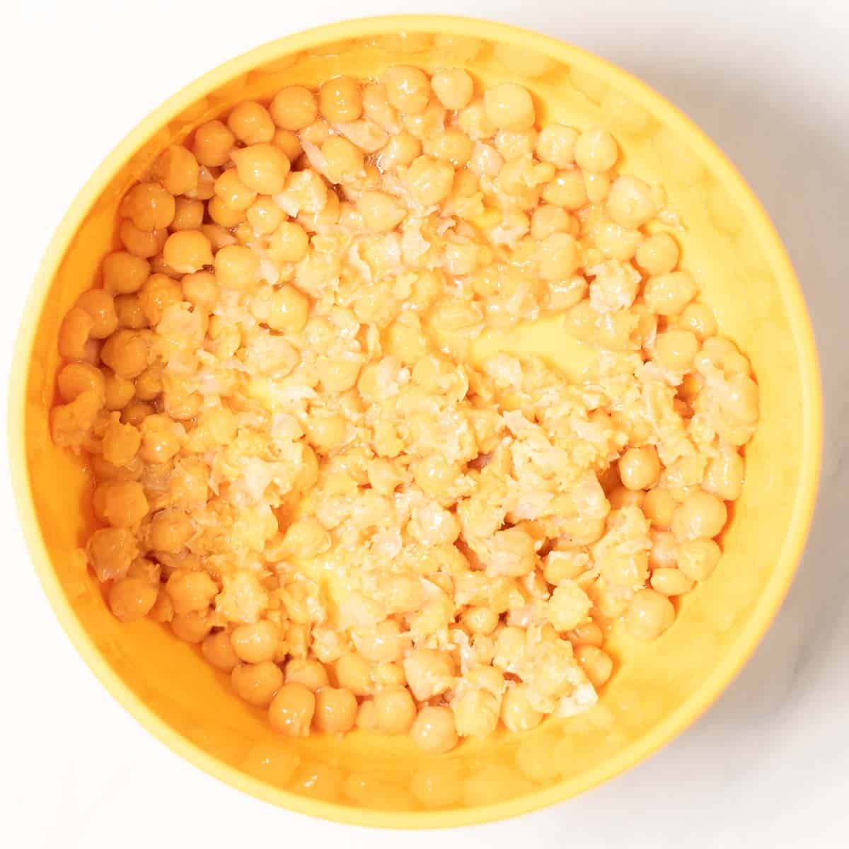 Chickpeas are slightly mashed in a mixing bowl.