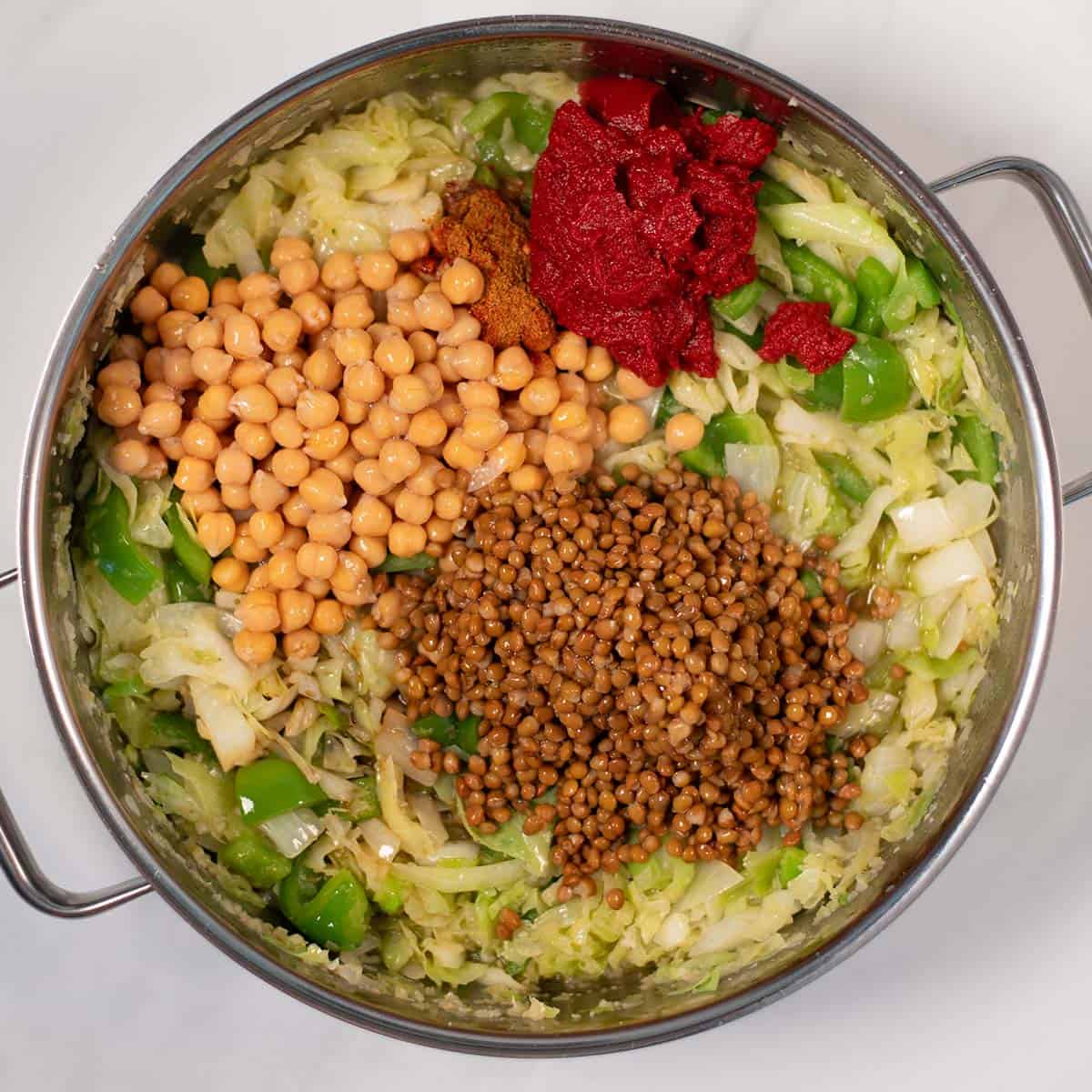 Chickpeas, lentils, tomato paste and spices are added to the pan.