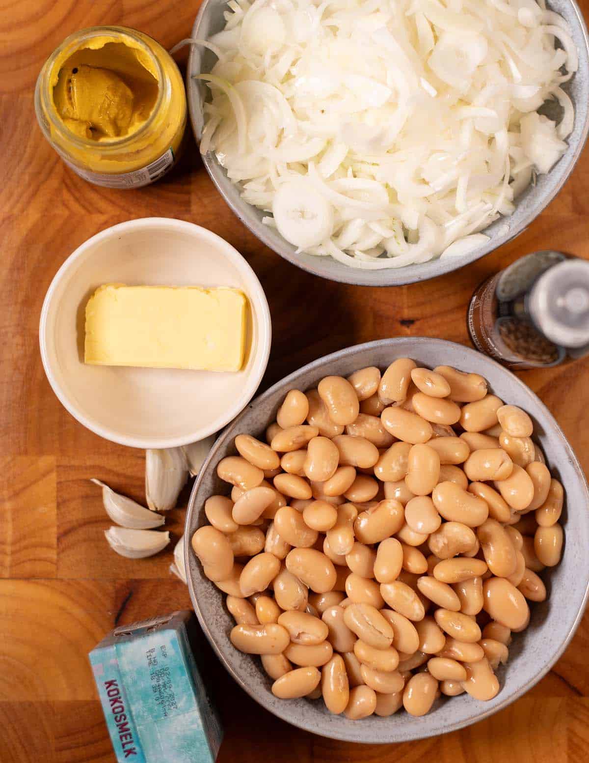 Ingredients needed to make French Onion Butter Beans collected on a board.
