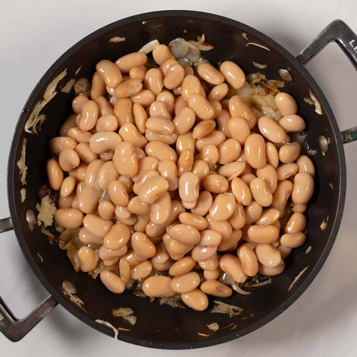 Butter beans are added to camramelized onions in a pan.