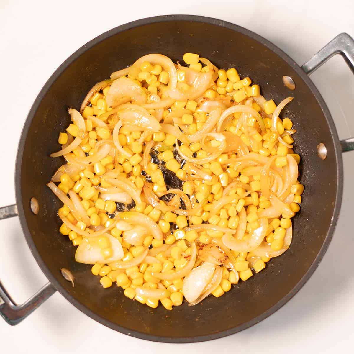 Onions and corn are roasted in butter in a pan.