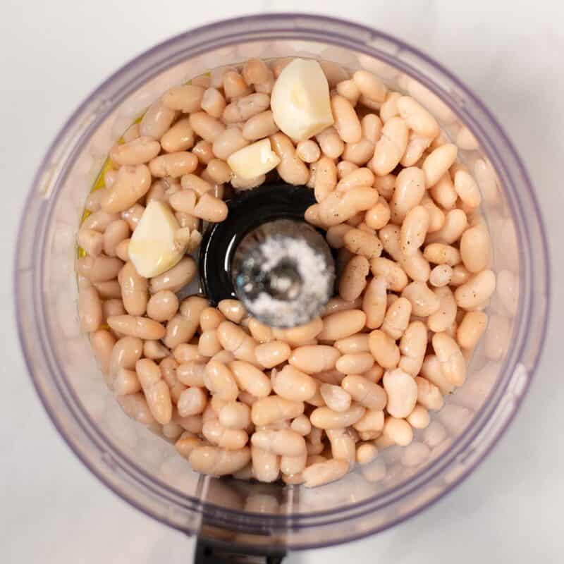 White beans and seasonings in the bowl of a food processor.