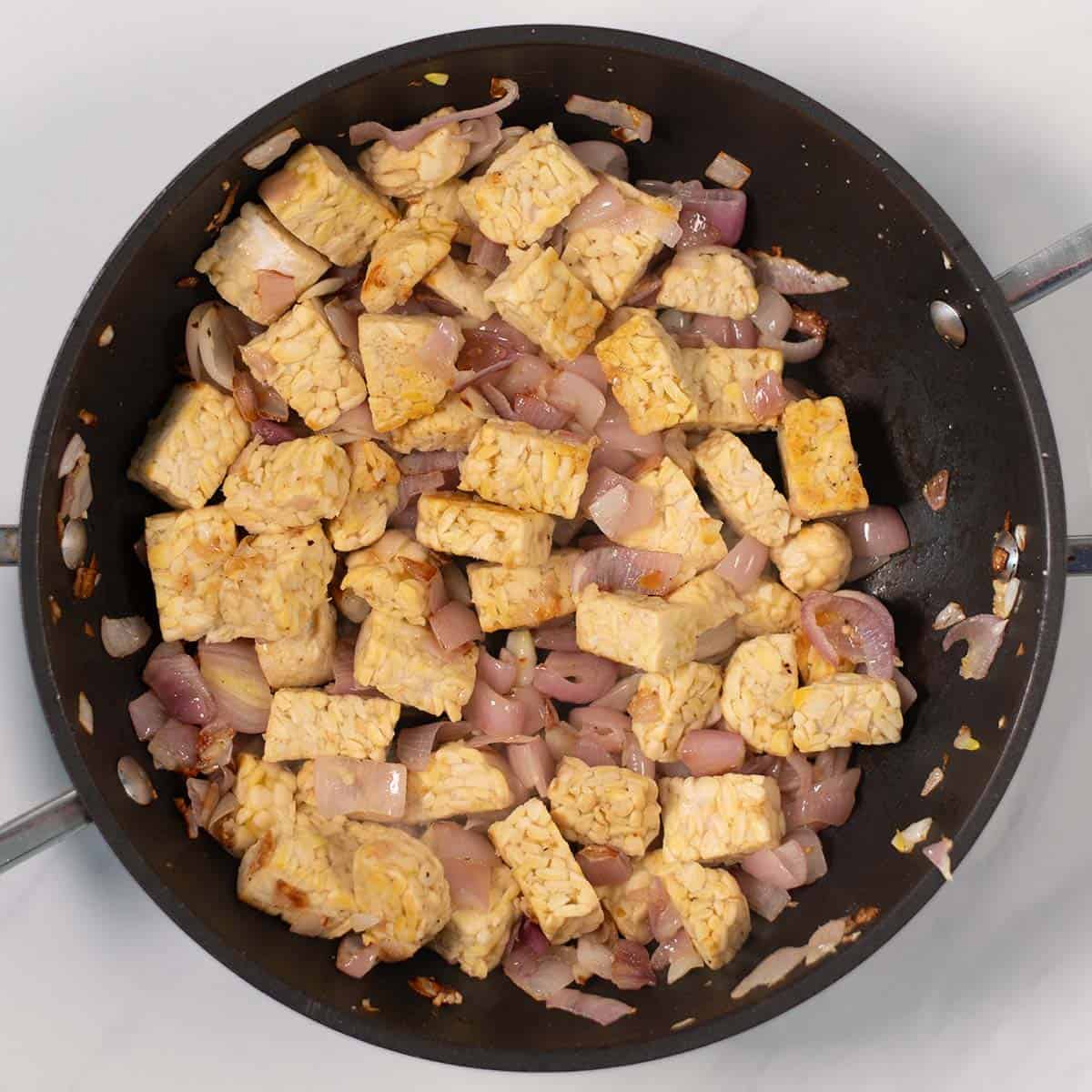 Tempeh and shallots are caramelized in a pan.