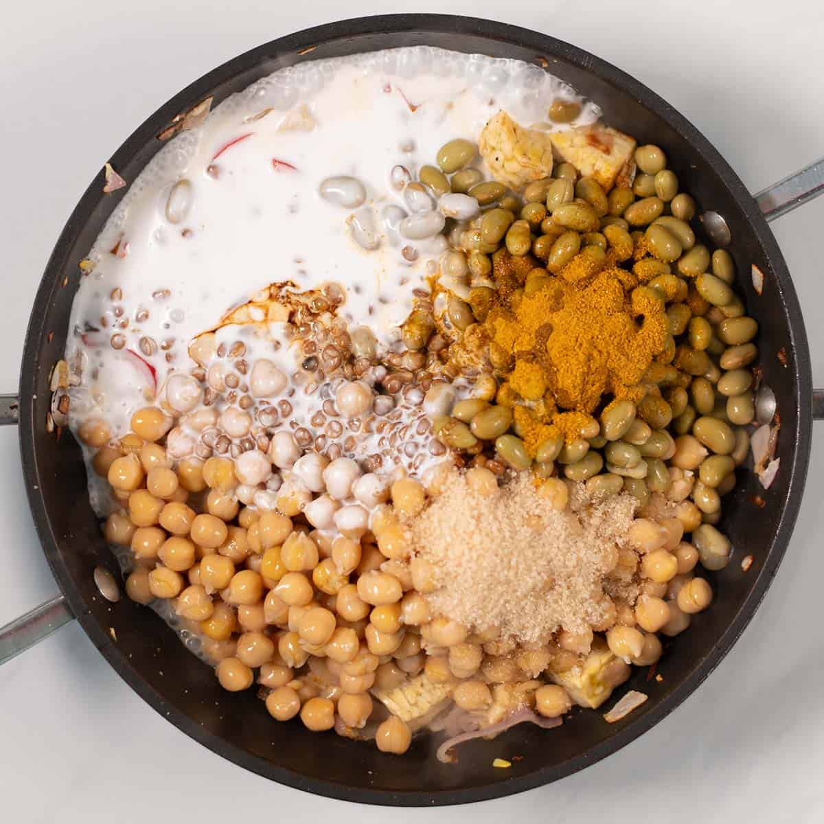Chickpeas, lentils, and curry ingredients are mixed with tempeh in a pan.