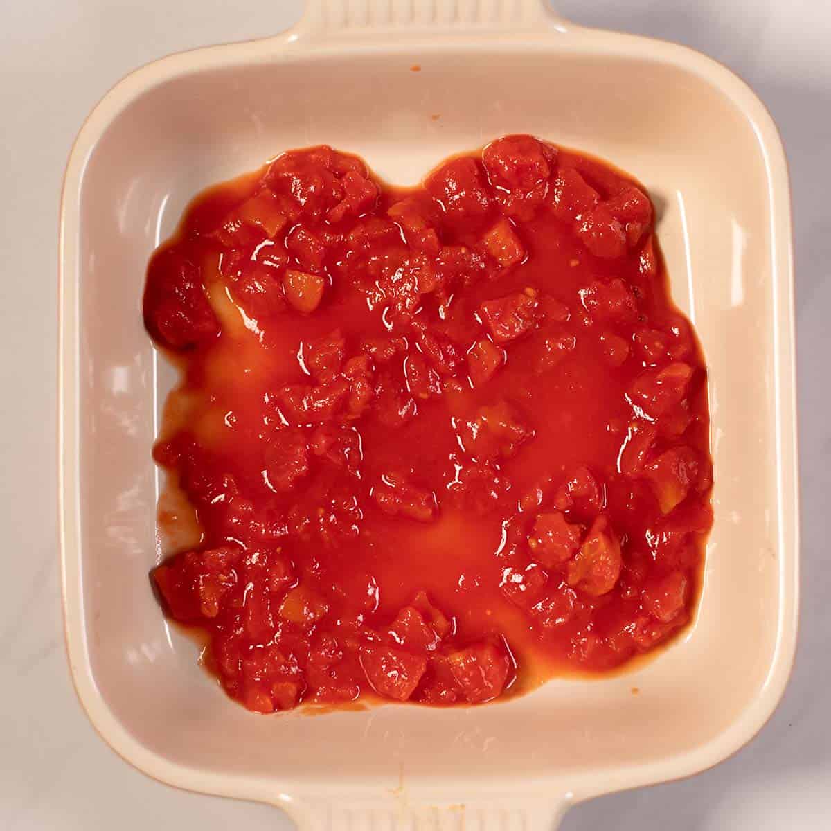 Diced tomatoes are layered into a baking dish.