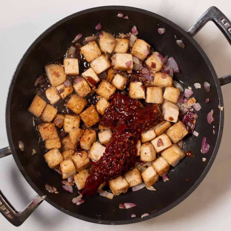 Chipotle peppers in abodo sauce are given to the tofu in the pan.